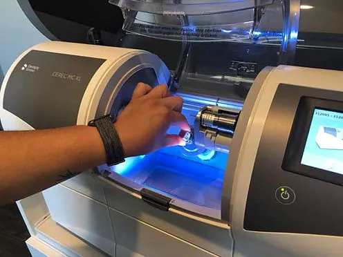 A technician loads a ceramic block into the CEREC MC XL milling machine at Crossroads Family Dental